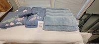 Blue towels laid out on a bed showing folded towels including embroidered hand and face towels and solid bath towels
