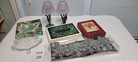 Full lot image showing green Christmas cards, glass tree dish, red tin can, lavender candle holders, silver tree ornaments, and other items arranged on white cloth.