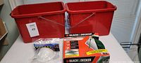 Two large red cleaning pails, box of Black & Decker 3-outlet power strip, and package of disposable masks on a white surface.