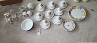 Photo of full dish set including dinner plates, small plates, cups with saucers, bowls, glasses, creamer, sugar, and salt and pepper shakers arranged on floor.