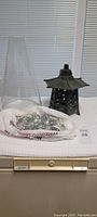 Photo showing the lantern chimney, bag of glass stones, and ceramic base with olive green lantern in the background