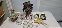 Wide shot of all candle holders, flower arrangement, and decorative container on table with blinds background