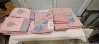 Full view of 12 stacked pink towels with kids-themed embroidered prints on some towels