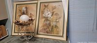Two gold framed artworks with matting leaning against wall, warm colour palette with nature and floral themes