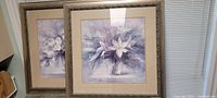 Two framed lilac themed artworks with taupe frames leaning against wall, view of both pieces together