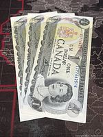 Front view of three consecutive 1973 Canadian one dollar banknotes stacked with visible portrait of Queen Elizabeth II and denomination.