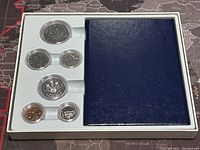 Full white plastic tray holding five Canadian coins in a specimen set and a blue pamphlet/booklet on the right side