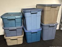 Photo showing seven Rubbermaid plastic storage containers stacked and arranged in two groups, displaying various blue and beige colors, lid styles, and sizes