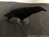 Side view of black metal crow sculpture showing detailed wing and tail etching, standing on a round metal base.