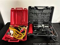 Two plastic cases; red case contains jumper cables and safety kit items, black case holds an air compressor and coiled air hose.