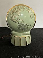Front view of the green world globe light showing raised continents and decorative base with gold accent.