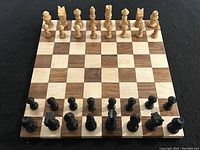 Full view of the chessboard set up with all black and natural wood chess pieces in starting positions.