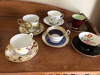 Six assorted bone china tea cup and saucer sets displayed on wooden surface