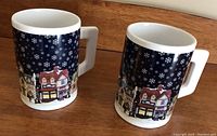 Pair of Christmas scene mugs with snowflake pattern and village illustration