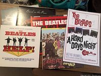 Photo showing six vinyl record covers and a laminated poster. Visible Beatles albums: Help!, A Hard Day's Night, Sgt. Pepper's Lonely Hearts Club Band, Band on the Run, plus a laminated poster for A Hard Day's Night.