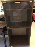 Front view showing glass doors with metal hinges and internal shelf, upper compartment for stereo equipment.