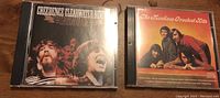 Two CD cases including Creedence Clearwater Revival and The Monkees Greatest Hits placed on wood surface.