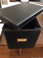 Black faux leather CD storage case with loose lid shown from above, label A-Be on front
