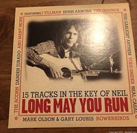 Cover of 'Long May You Run' CD featuring black-and-white photo of man playing guitar and artists names around the border