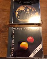 Two Paul McCartney CDs, 'Band on the Run' and 'Venus and Mars', shown in jewel cases on wood surface.