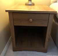 Close-up side view of an oak wood veneer end table showing single drawer with wooden knob and open bottom shelf.