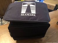 Closed navy blue fabric cooler bag, front displaying the Seamark logo with white lighthouse design.