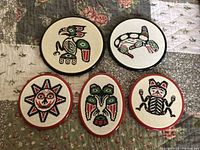 Five circular embroidered Indigenous wall hangings showing animals and sun motif in red, green, black, white, framed with colored rims