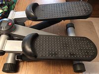 Close-up side view of the two large black textured foot pedals with nubs, silver metal frame, and part of the adjustable tension knob.