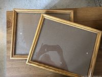 Top view of two oak finished picture frames laid on wooden surface showing front glass and wooden edges