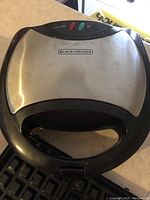 Top view of the grill closed showing brushed stainless steel top with Black & Decker logo and black plastic handle.