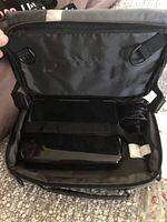 Closed black nylon carrying case with zipper showing some contents including power cables and the folded DVD player inside.