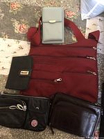 Set of travel purses includes red canvas crossbody bag with multiple zippered pockets, black passport holder, grey phone case, and two small black wallet-style bags with various compartments.