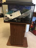 Front view of 10 gallon aquarium with black rim, some accessories inside and wooden stand beneath