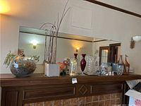 Photo of mantelpiece showing multiple decor pieces including wooden giraffe, glass vases, dome clock, and other items
