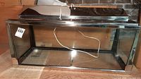 Front view of glass aquarium tank showing metal frame and attached black metal top light with power cord inside tank
