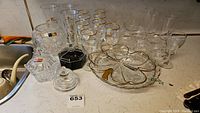 Wide shot of crystal and glassware items on counter including pinwheel bowl, black Arcoroc bowl, decanter, glasses with gold rims and cut crystal bowls