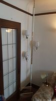 Floor to ceiling mid-century modern lamp with three glass light covers and brass-colored magazine rack at base