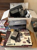 Box partially opened showing various vintage electronic items including radios and tape deck, Uniden phone box in foreground