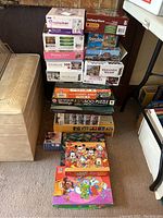 Stack of assorted 500 and 1000 piece puzzles with boxes showing various themes and brands