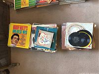 Top view of three stacks of vintage vinyl records on the floor, showing album covers including Buddy Holly's Greatest Hits and other assorted records.