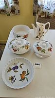 Five porcelain serving pieces on white cloth, with fruit motif designs