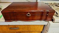 Closed wooden chest with brass handle for storing silverplate flatware.
