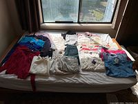 Wide view of all women's clothing laid out on a bed, including sweaters, tops, pants, skirts, and jackets, showing the quantity and variety of pieces.