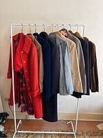 Front and side view of 9 vintage women's coats on rack, showing variety of colors and styles.