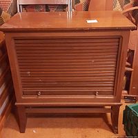 Full front view of the wood cabinet showing roll-up door and slight wear on surface.