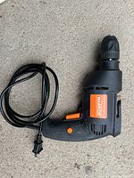 Black and orange WARRIOR corded drill with hand-locking chuck and power cord coiled beside it on concrete floor.