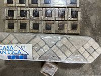 Close-up of beige and brown mosaic accent tile piece with geometric pattern and wrapped tile tool below it