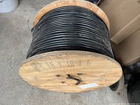 Wooden spool wound with black insulated wire, showing the spool's construction and wire thickness.