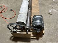 Side view of tumbler showing belt drive motor, rotating shaft, and one PVC pipe container mounted on wooden pallet