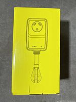 Photo of yellow box packaging displaying a schematic image of the surge protector device showing the plug and socket.
